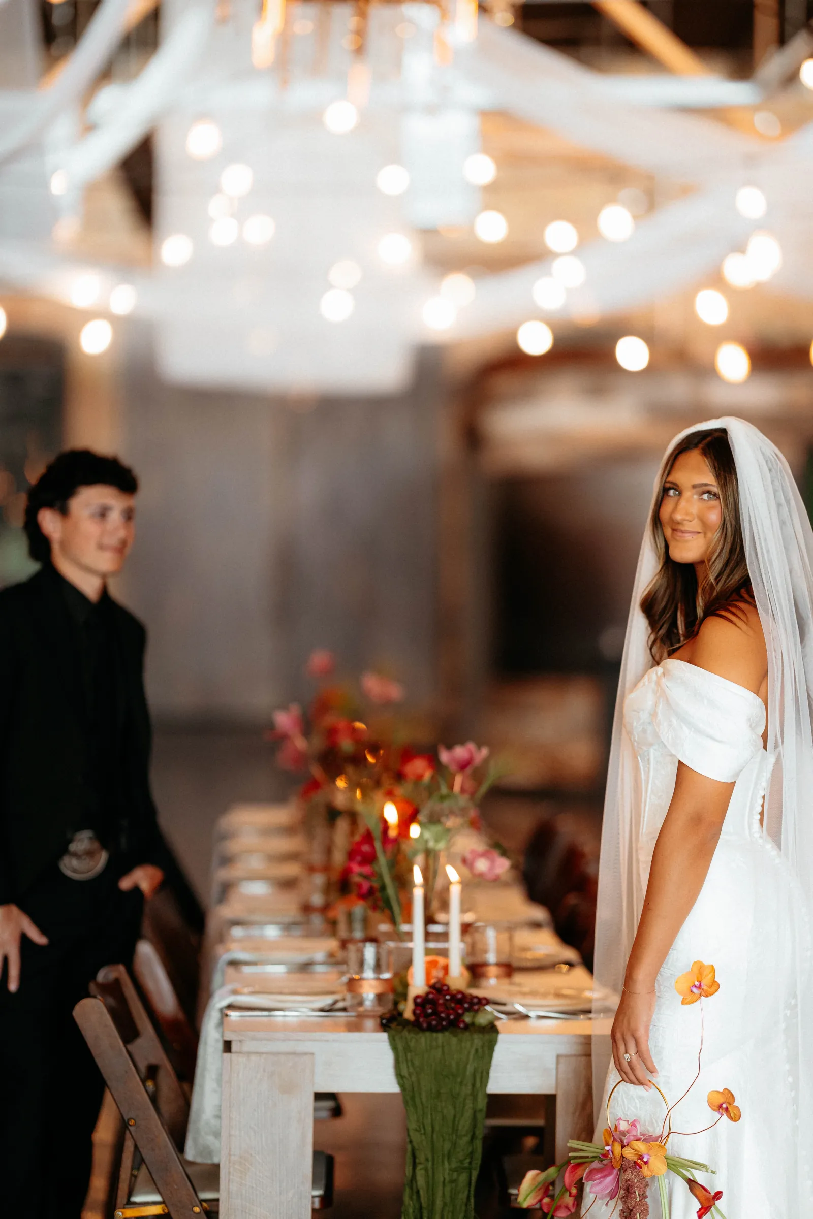 Bride looking back over a long set table under string lights